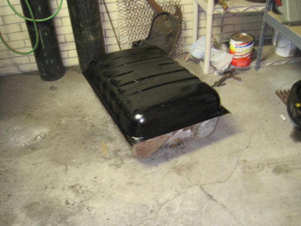 black fuel tank sitting on concrete floor, next to a green hose and a metal tank