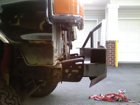 1990 Ford Bronco - Low-angle shot of a bare-metal fabricated front bumper with a stinger hoop being test-fitted to the frame horns of a truck in a driveway, w…