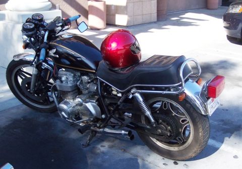 1999 Ford Crown Victoria - A black motorcycle with chrome accents and a red helmet rests on its kickstand.