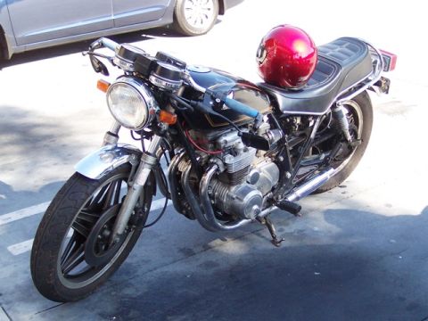 1999 Ford Crown Victoria - A black motorcycle with a red helmet rests on its seat, parked outdoors next to a silver car.