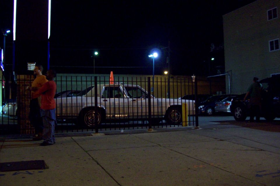 Light-colored two-door sedan on chrome wheels parked in lot at night