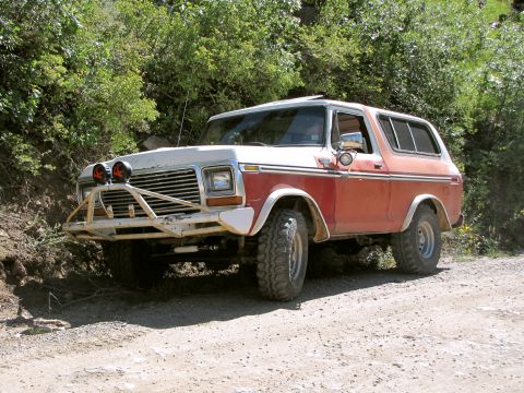 1978 Ford Bronco - Two-tone red and white full-size Ford Bronco with brush guard, off-road tires and lift, parked on a dirt trail.