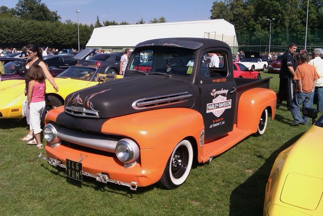 Two-tone orange and black 1950 Ford F-Series pickup truck with Harley-Davidson livery, parked on grass at a car show