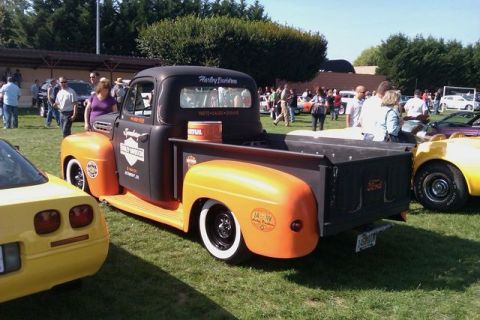 1991 Ford Crown Victoria - A customized black and orange Ford F-Series pickup truck, likely from the early 1950s, is displayed at a car show next to a yellow Corvette.