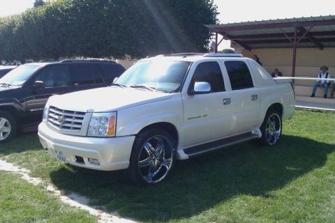1991 Ford Crown Victoria - A white Cadillac Escalade EXT is parked on a grassy area next to another vehicle.