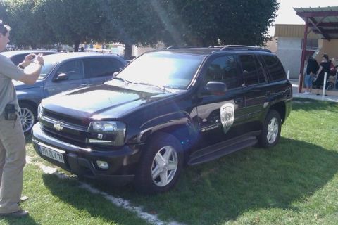 1991 Ford Crown Victoria - A black SUV with a shield emblem on the door is parked on a grassy area, with another vehicle visible behind it.