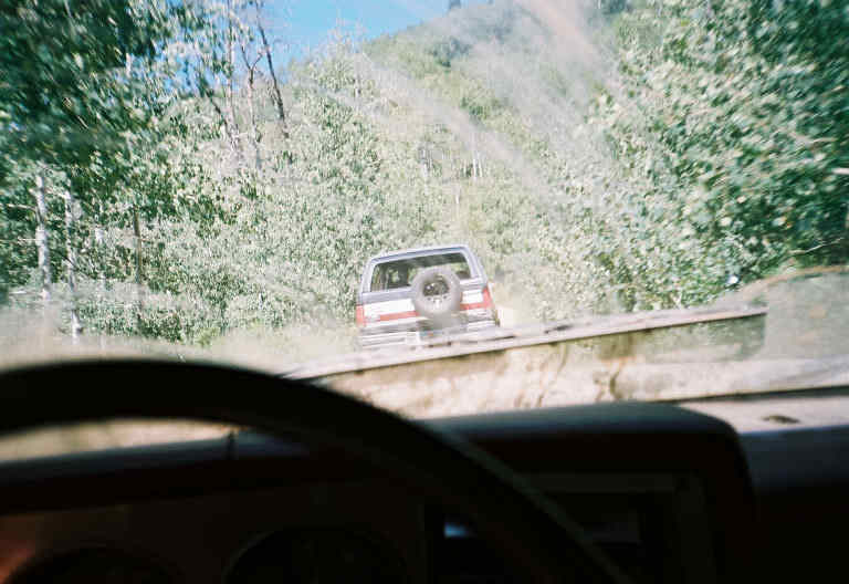 SUV with spare tire on back driving up a dirt road, seen from inside another vehicle