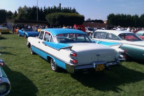 1991 Ford Crown Victoria - A classic two-tone sedan with prominent tail fins is displayed at an outdoor event with other vehicles present.