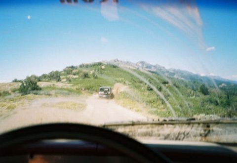 1991 Ford Bronco - An SUV navigates a dusty trail through a hilly, green landscape under a clear blue sky.