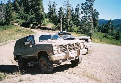 1991 Ford Bronco - Two SUVs parked on a dirt road in a wooded, mountainous area.