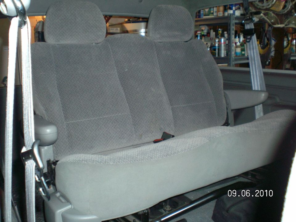 Gray cloth rear bench seat with headrests installed in a vehicle, garage shelving behind