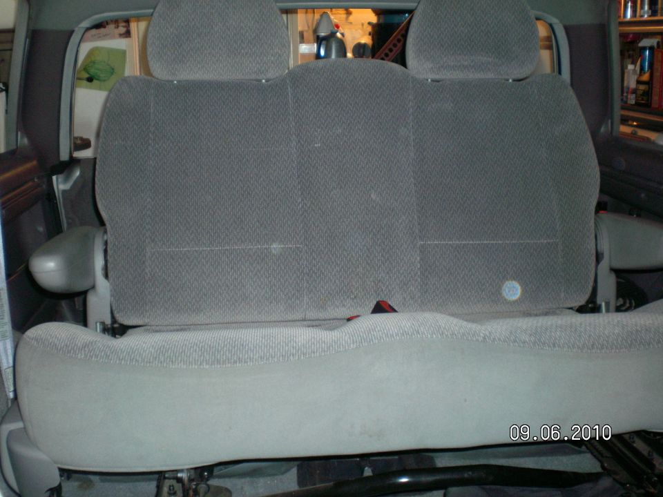 Gray fabric rear seat with three headrests and a seatbelt buckle visible