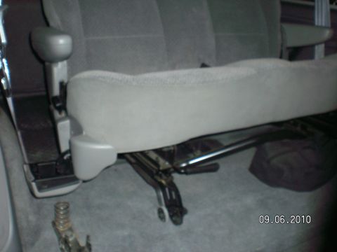 1996 Ford Bronco - Gray cloth bench seat sitting inside a vehicle with its folding legs and latch hardware extended below the cushion, resting on gray carpet.…