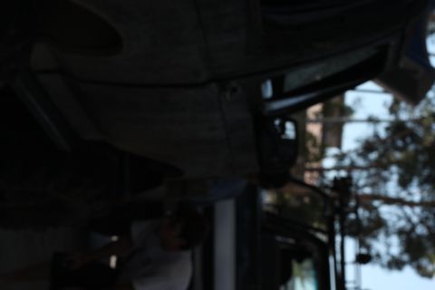 1992 Ford Bronco - A person works on the underside of a vehicle, with trees and buildings in the background.
