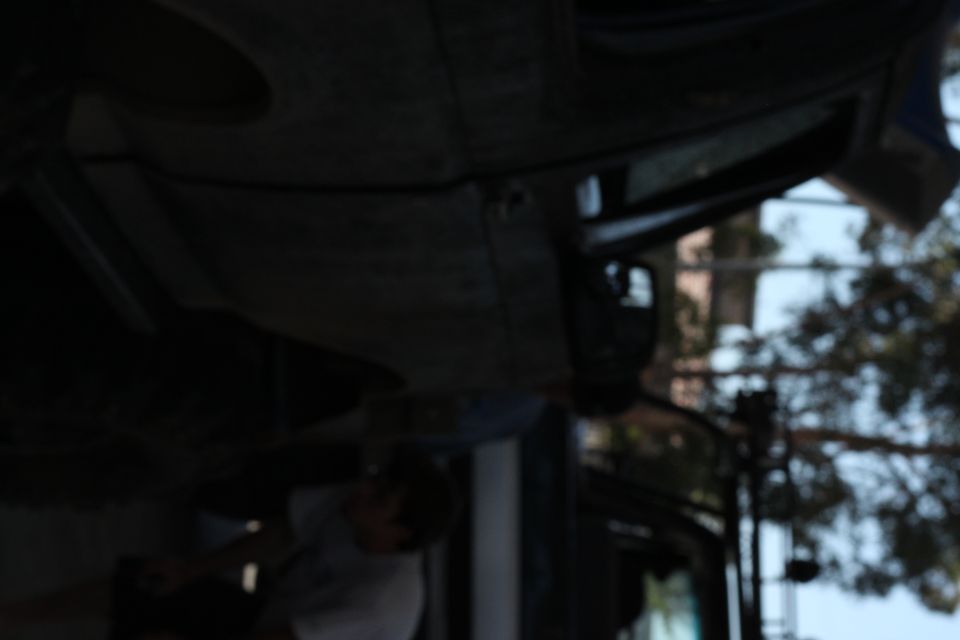 Underside of a dark-colored vehicle, viewed from below, with a person visible in the background