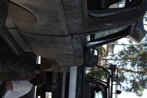 1992 Ford Bronco - A person examines the underside of a heavily soiled vehicle, with a tire and body panel visible.