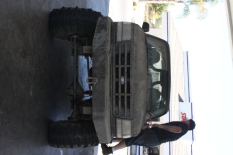 1992 Ford Bronco - A man works on a muddy 1992 Ford Bronco with oversized tires.