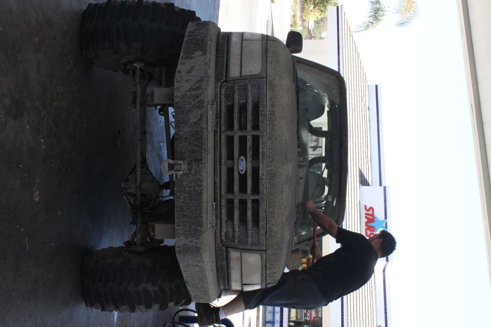 Man works on front of lifted Ford truck with large tires. Grille has Ford logo