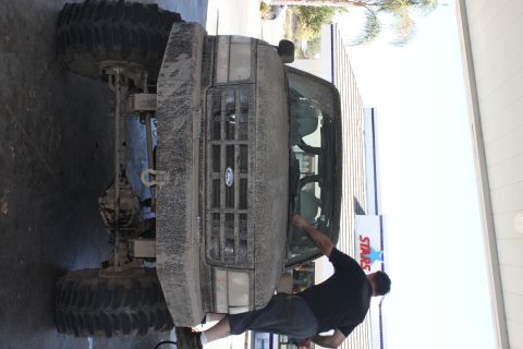 1992 Ford Bronco - A man cleans the windshield of a mud-splattered 1992 Ford Bronco parked outdoors.