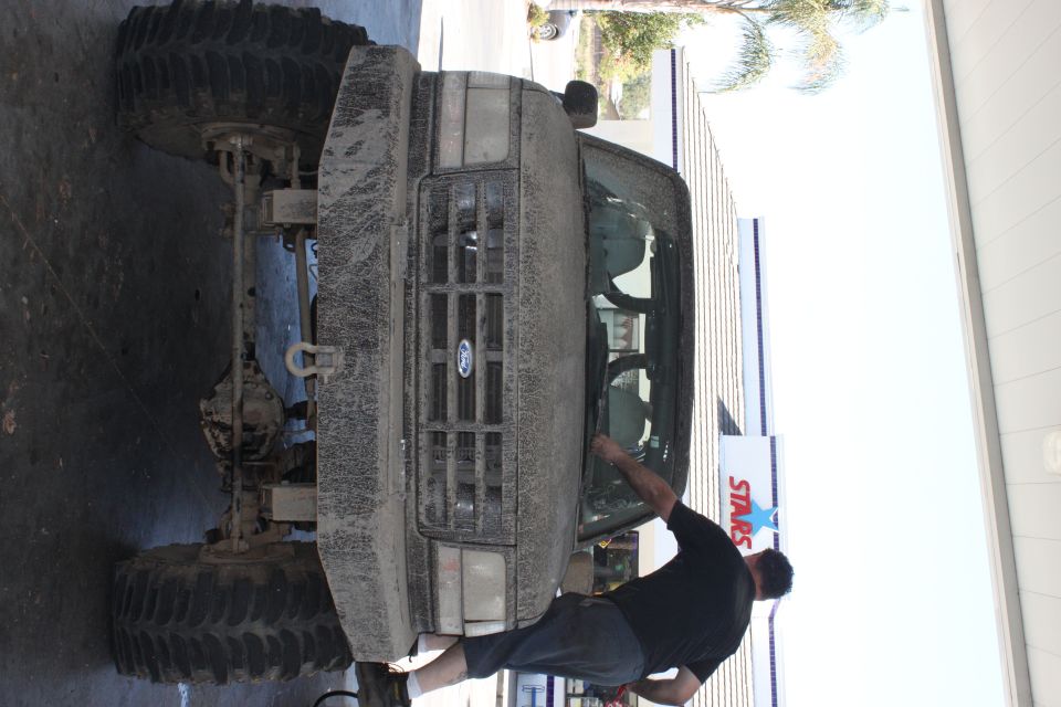 Mud-covered 1992 Ford Bronco front view with large tires and a man cleaning the windshield