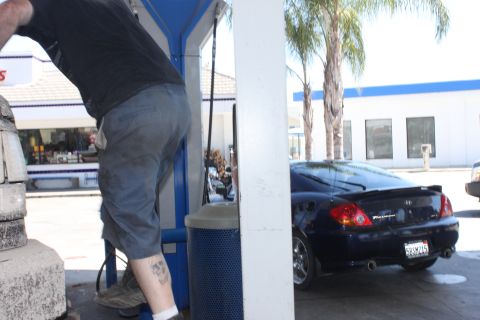 1992 Ford Bronco - A dark coupe is seen from the rear at a gas station, with a person visible near the pump.