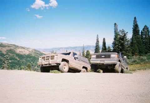 1991 Ford Bronco - Two SUVs are parked on a dirt road in a mountainous area under a clear blue sky.