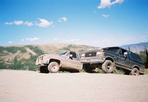 1991 Ford Bronco - Two trucks are parked on a dirt road in a hilly, outdoor landscape under a blue sky.