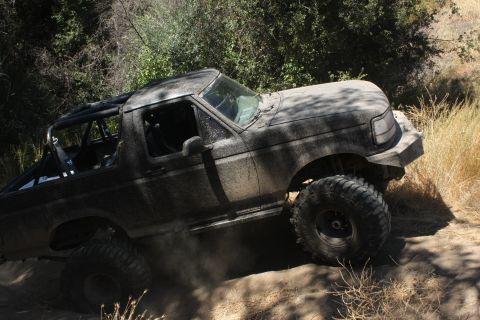 1992 Ford Bronco - This heavily modified off-road vehicle is kicking up dust as it navigates a steep, dry trail.