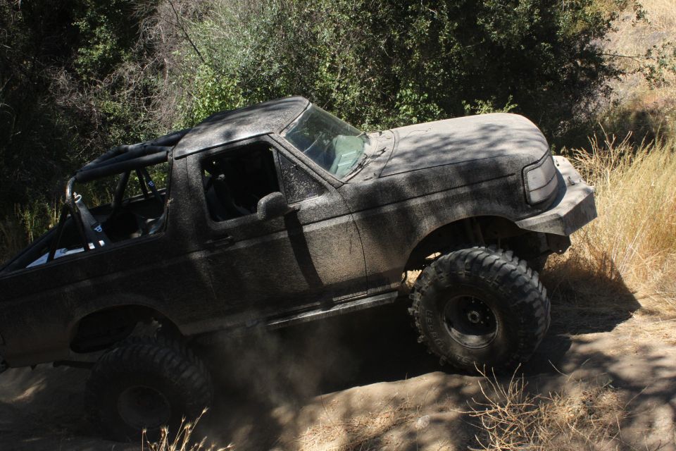 Mud-covered off-road vehicle climbing a dirt hill with large tires and a roll cage