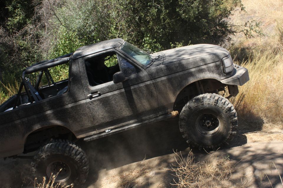 1992 Ford Bronco covered in mud, driving on a dirt trail with large off-road tires