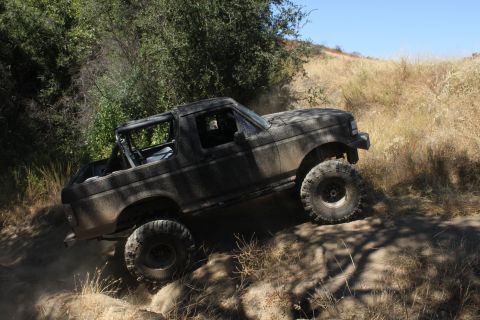 1992 Ford Bronco - A dusty 1992 Ford Bronco navigates a challenging off-road trail with steep inclines.