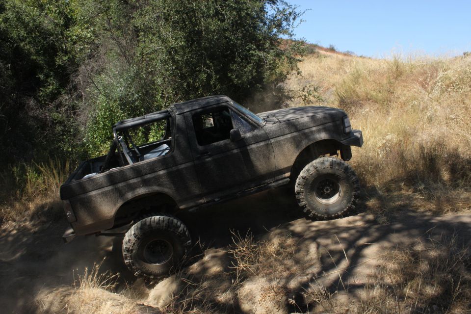 Black 1992 Ford Bronco off-roading on a dirt trail, covered in dust