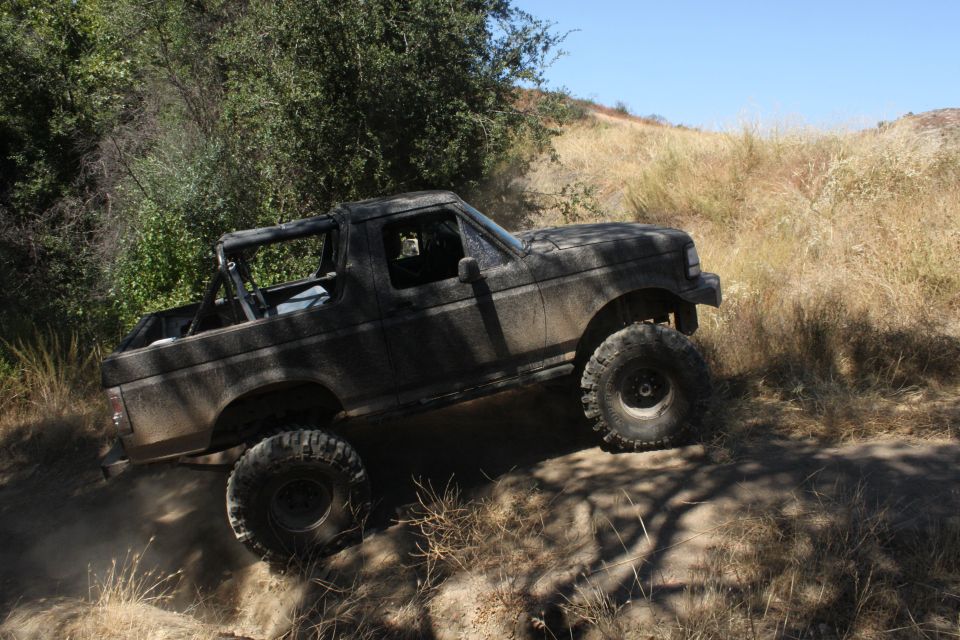 1992 Ford Bronco off-roading on a dusty trail with large tires