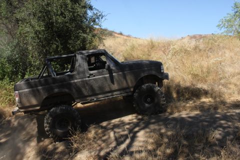 1992 Ford Bronco - This modified SUV is navigating a dusty trail under a clear blue sky.