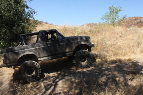 1992 Ford Bronco - This 1992 Ford Bronco is shown off-road on a dusty trail with dry grass and trees.