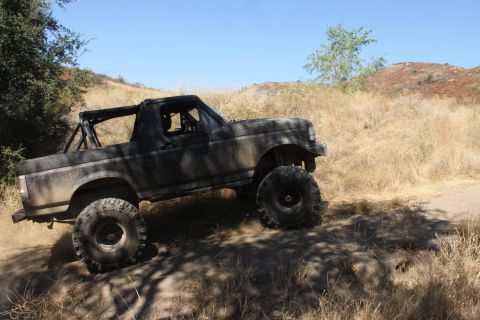 1992 Ford Bronco - Modified 1992 Ford Bronco tackles an off-road trail under a clear blue sky.