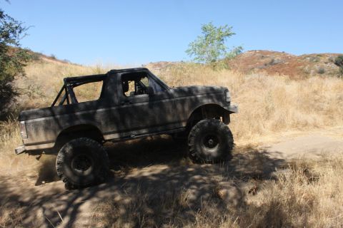 1992 Ford Bronco - A SUV navigates a dusty, off-road trail under a clear blue sky.