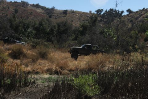 1992 Ford Bronco - Two off-road vehicles navigate a dry, overgrown terrain under a clear sky.