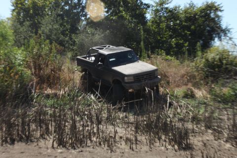 1992 Ford Bronco - This 1992 Ford Bronco navigates a challenging off-road path through dense vegetation and mud.