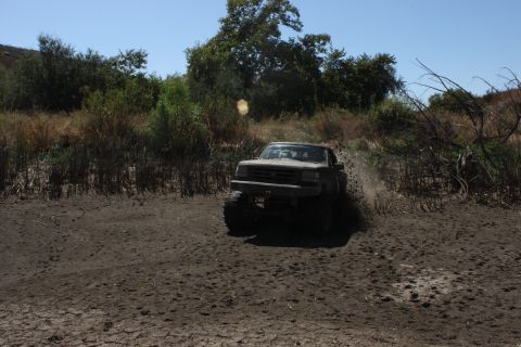 1992 Ford Bronco - Ford Bronco navigating a muddy trail with trees and dry brush in the background.