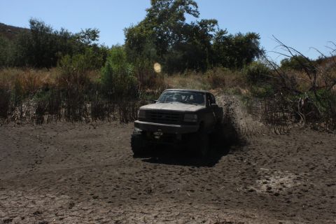 1992 Ford Bronco - A lifted truck navigates a muddy trail, sending dirt flying.