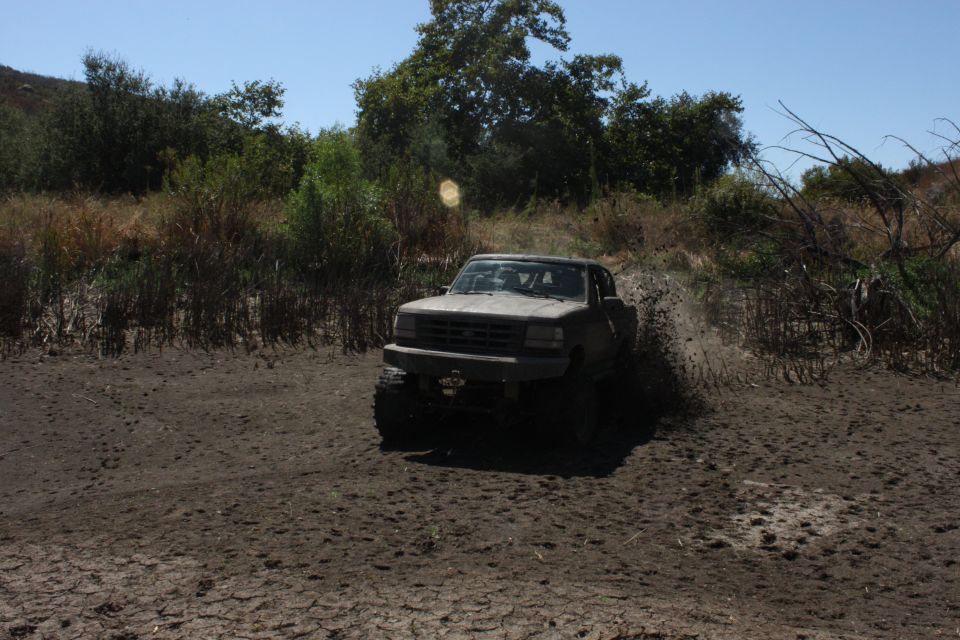 Truck driving through mud, kicking up dirt. Trees and brush in background