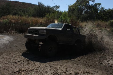 1992 Ford Bronco - A 1992 Ford Bronco navigates a muddy trail, sending dirt flying.