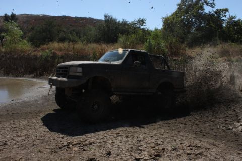 1992 Ford Bronco - A 1992 Ford Bronco navigates a muddy trail, sending dirt flying.