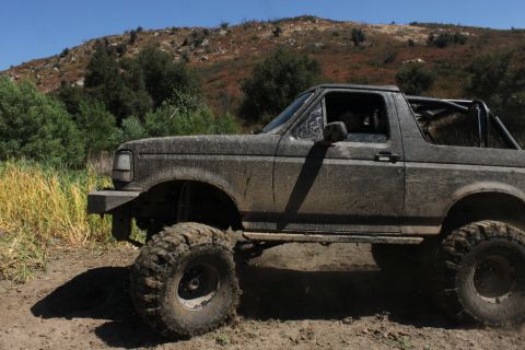 1992 Ford Bronco - 1992 Ford Bronco navigating a muddy trail with large tires and a roll cage visible.
