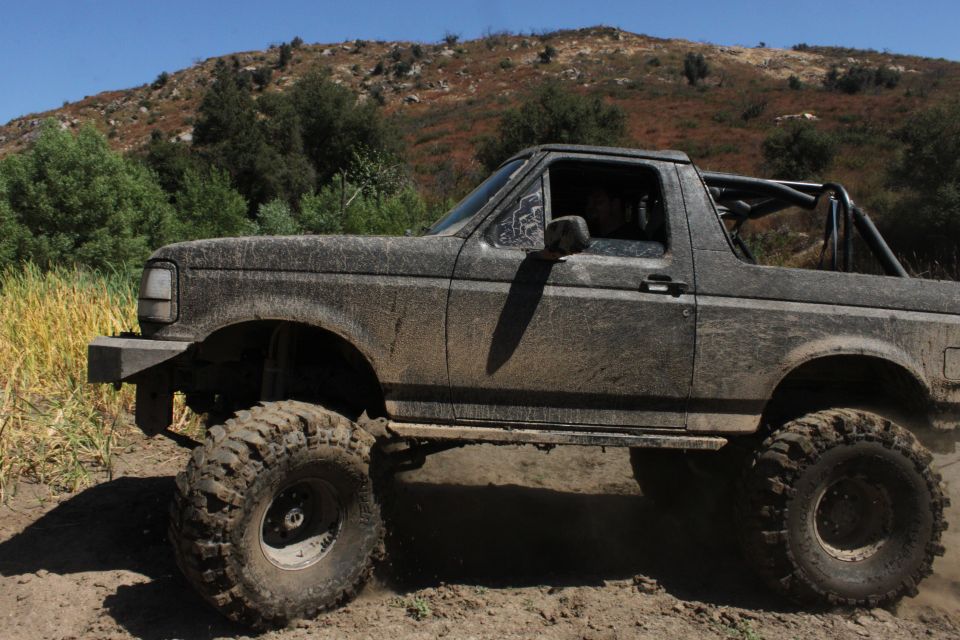 Muddy 1992 Ford Bronco with large tires on a dirt trail, hills in background