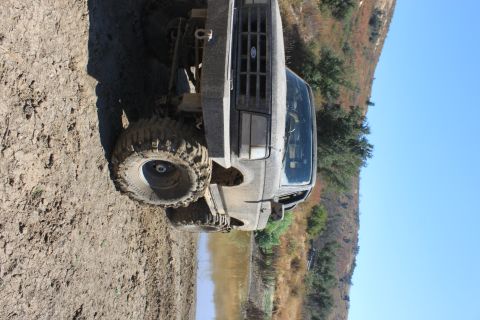 1992 Ford Bronco - This heavily modified truck is shown off-road, covered in mud, with a clear blue sky above.