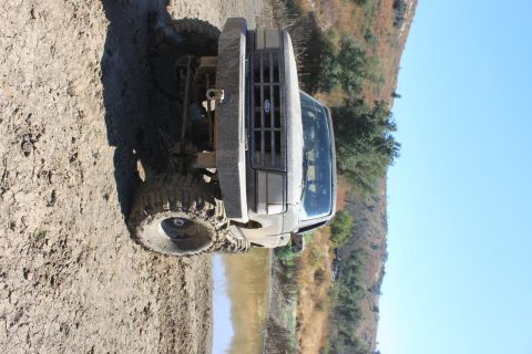 1992 Ford Bronco - A 1992 Ford Bronco is seen from the front, partially submerged in mud on a trail.