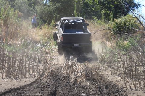 1992 Ford Bronco - A black off-road truck navigates a muddy, overgrown trail, kicking up dust as it goes.