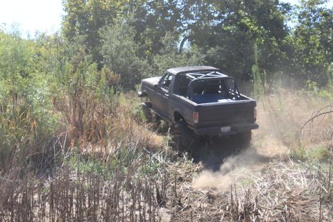 1992 Ford Bronco - A 1992 Ford Bronco kicks up dust as it navigates a rough, overgrown trail.